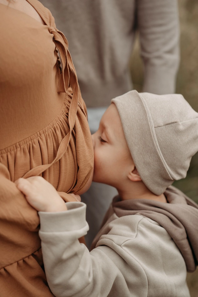 Am Bild sieht man eine Detailaufnahme. Ein Kind gibt seiner Mutter einen Kuss auf deren Babybauch.