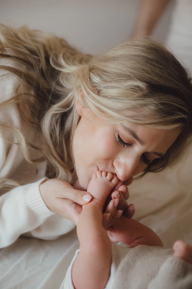 Auf dem Bild sieht man eine Mutter wie sie ihrem Baby einen Kuss auf den Fuß gibt.