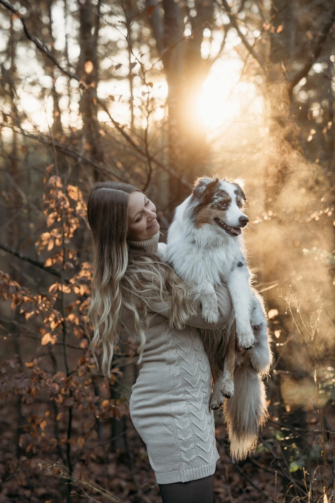 Am Bild sieht man eine Frau und ihren Hund im Sonnenuntergang. Sie hält ihren Hund in den Armen und lächelt ihn an.